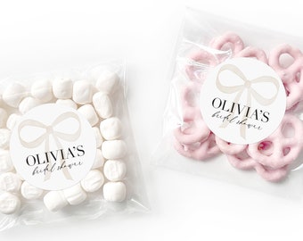 Könnte beinhalten: Zwei durchsichtige Plastiktüten gefüllt mit Partygeschenken. Eine Tüte enthält weiße Marshmallows mit einem runden Aufkleber, auf dem "Olivia's bridal shower" mit einer weißen Schleife steht. Die andere Tüte enthält rosa Brezelbissen mit einem runden Aufkleber, auf dem "Olivia's bridal shower" mit einer weißen Schleife steht.