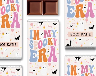 May include: Multiple chocolate bars wrapped in light pink paper featuring the text IN MY SPOOKY ERA in blue, orange, and pink bubble letters. The design includes small illustrations of white ghosts, black bats, orange candy corn, and pink lollipops.
