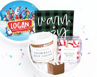 May include: A white gift box filled with holiday treats. Includes a jar of Snowball Hot Cocoa, a chocolate spoon, and a box of Holiday Mints. The lid features a Santa Claus illustration with the name "Logan" and the words "Merry Christmas".