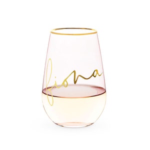K&ouml;nnte beinhalten: Ein klares Weinglas aus Glas mit goldenem Rand und dem Namen "Fiona" in goldener Schrift auf der Seite. Das Glas ist mit einem hellen Getr&auml;nk gef&uuml;llt.