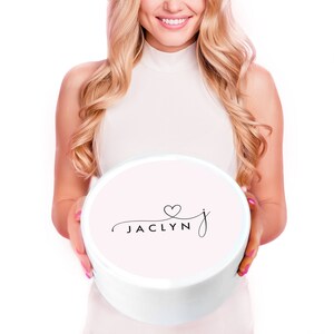 Puede incluir: Una caja redonda blanca con una tapa rosa. La tapa tiene una fuente cursiva negra que dice "Jaclyn" con un peque&ntilde;o coraz&oacute;n sobre la "J".