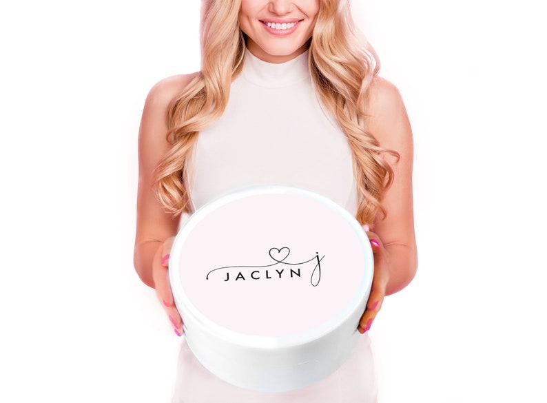 Puede incluir: Una caja redonda blanca con una tapa rosa. La tapa tiene una fuente cursiva negra que dice "Jaclyn" con un peque&ntilde;o coraz&oacute;n sobre la "J".