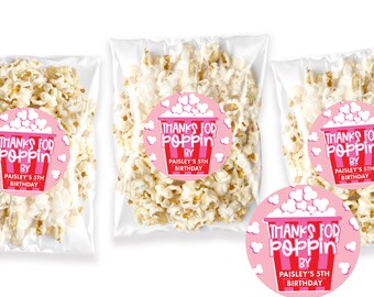 May include: Pink and red round favor tags with the text "Thanks for Poppin' by Paisley's 5th Birthday" and a cartoon popcorn bucket. The tags are attached to clear plastic bags filled with popcorn.