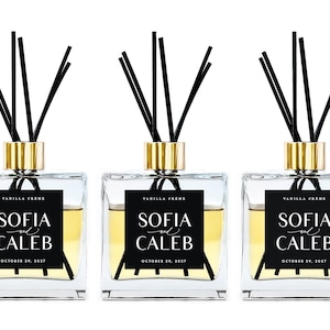 May include: Three clear glass bottles with gold lids and black diffuser sticks. Each bottle has a black label with white text that reads "Vanilla Creme", "Sofia and Caleb", and "October 29, 2027".