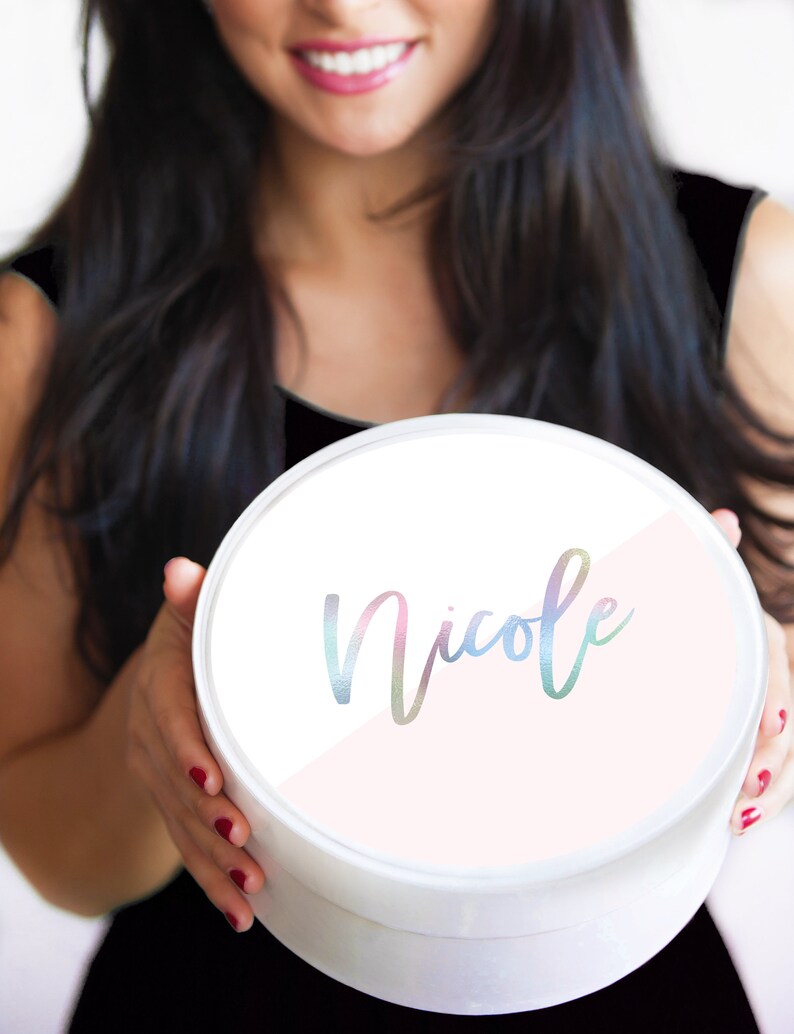 May include: A white round gift box with a pink and white design. The name "Nicole" is written in a rainbow iridescent font on the box.