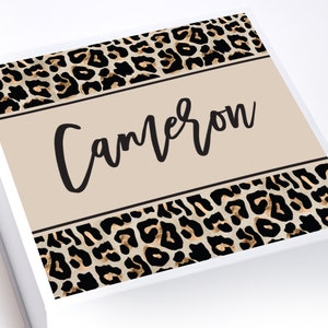 May include: A white gift box with a leopard print design and the name "Cameron" printed on the front.
