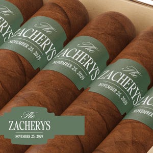 May include: Close-up of cigars in a box. Each cigar is wrapped in brown paper and has a green label with the text "The Zacherys" and "November 25, 2029". The cigars are arranged in a row.