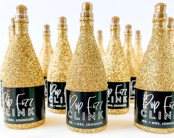 May include: Gold glitter champagne bottles with black labels that say "Pop Fizz Clink" and "Mr. & Mrs. Johnson".