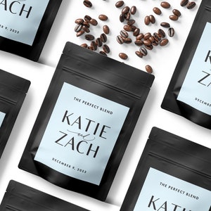 Puede incluir: Tres bolsas de caf&eacute; negras con etiquetas blancas. Las etiquetas tienen un fondo azul claro y dicen "The Perfect Blend" con los nombres "Katie y Zach" y la fecha "December 9, 2023".