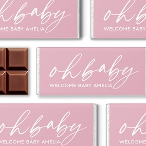 May include: Pink chocolate bar wrappers with the text "oh baby" and "WELCOME BABY AMELIA" in white script. A section of a brown chocolate bar is visible on the left. The wrappers are arranged in a grid pattern.