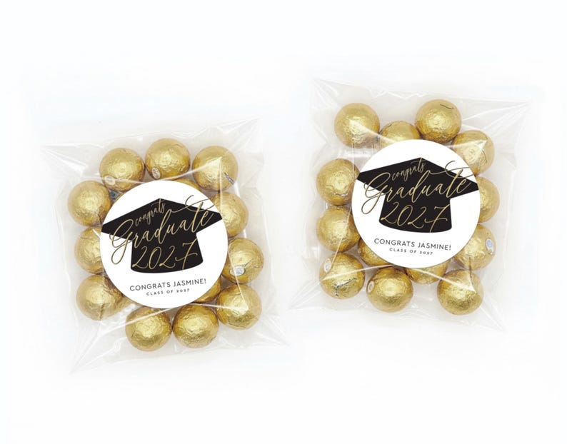 May include: Two clear cellophane bags filled with gold-wrapped candies. Each bag has a round sticker with the text "Congrats Jasmine! Graduate 2027" in black and gold script and a graduation cap illustration.