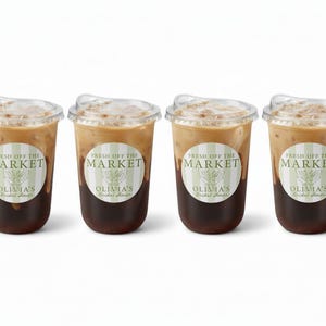 May include: Four iced coffee drinks in clear plastic cups with lids. Each cup has a sticker that reads "FRESH OFF THE MARKET" and "OLIVIA'S Bridal Shower". The coffee is layered with a dark brown base and a lighter, creamy top.