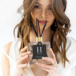 May include: A square glass reed diffuser bottle with a gold collar and black reeds. The front features a black square label with a white letter H, the text HILTON, and the words VANILLA CREME REED DIFFUSER printed in white lettering.