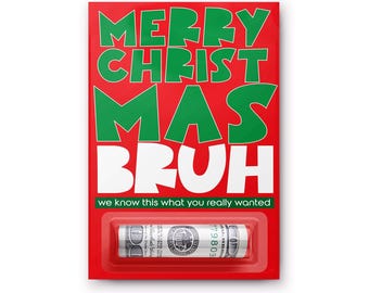 Puede incluir: Una tarjeta rectangular roja con el texto verde MERRY CHRISTMAS y el texto blanco BRUH. Debajo, el texto dice WE KNOW THIS WHAT YOU REALLY WANTED. Un blíster de plástico transparente en la parte inferior contiene un billete de cien dólares enrollado.