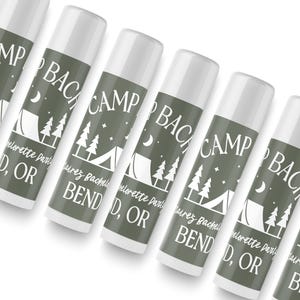May include: A set of six green and white lip balm tubes with the text "Camp Bachelorette Party Bend, OR" printed on each tube. The tubes feature a camping tent, trees, and stars.