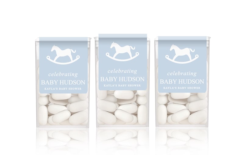 May include: Three clear containers of white mints with blue and white labels. The labels feature a white rocking horse and the text "celebrating Baby Hudson Kayla's Baby Shower".