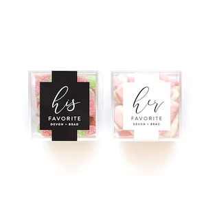 May include: Two square clear plastic boxes filled with colorful gummy candies. The left box has a black label with white text reading his FAVORITE DEVON + BRAD. The right box has a white label with black text reading her FAVORITE DEVON + BRAD.