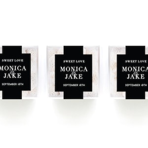 May include: Three clear square boxes filled with small white candies, each wrapped with a black paper band featuring the white text SWEET LOVE, MONICA & JAKE, and SEPTEMBER 18TH printed in a clean, centered serif font on the front of the boxes.