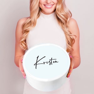 May include: A white round box with a light blue lid. The lid has the name "Kristen" written in black cursive.