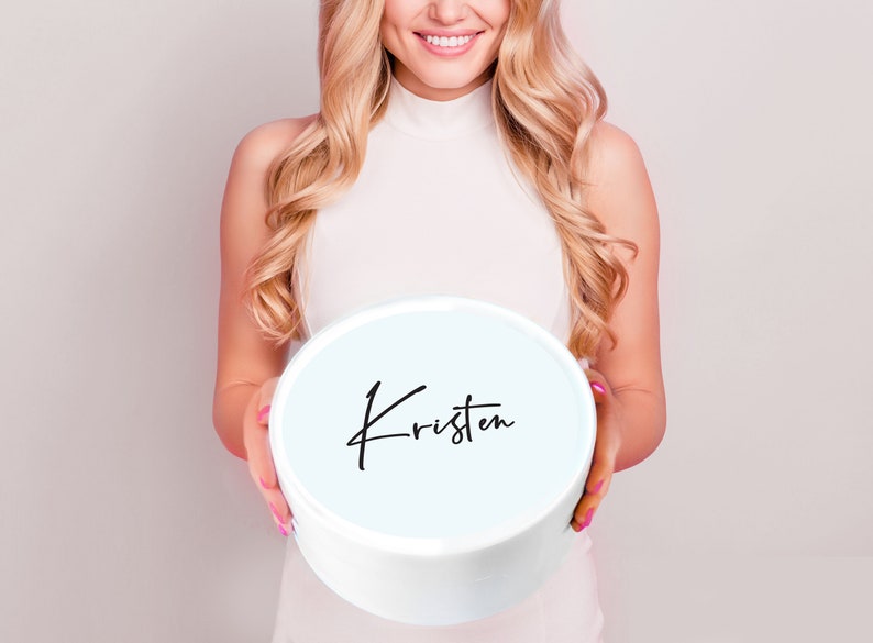 May include: A white round box with a light blue lid. The lid has the name "Kristen" written in black cursive.