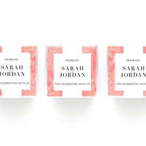 May include: Three small pink and white boxes with clear lids. Each box has a white label with the text "Thank you Sarah & Jordan for celebrating with us".