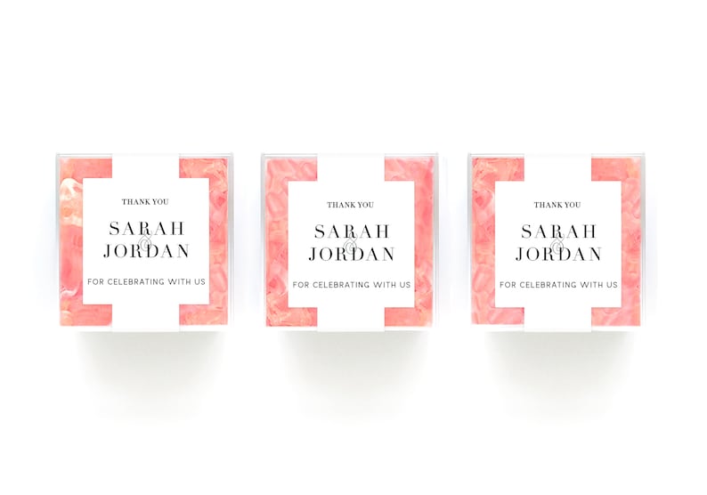 May include: Three small pink and white boxes with clear lids. Each box has a white label with the text "Thank you Sarah & Jordan for celebrating with us".
