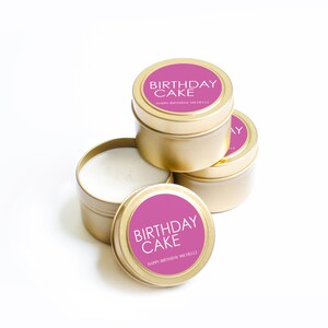 以下が含まれることがあります： ピンクのラベルが付いた金色のキャンドル缶が4つ。ラベルには「Birthday Cake」と「Happy Birthday Michelle」と書かれています。