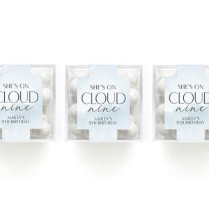 May include: Three clear square boxes filled with white candies. Each box has a label that reads "She's on Cloud Nine" and "Ashley's 9th Birthday" in a soft blue font. The boxes are arranged on a white background.