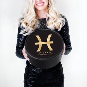 K&ouml;nnte beinhalten: Eine schwarze runde Box mit einem goldenen Fische-Sternzeichen und dem Text "Pisces Valerie | February 22".