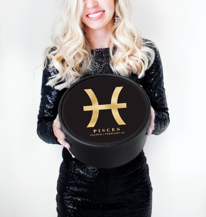 K&ouml;nnte beinhalten: Eine schwarze runde Box mit einem goldenen Fische-Sternzeichen und dem Text "Pisces Valerie | February 22".