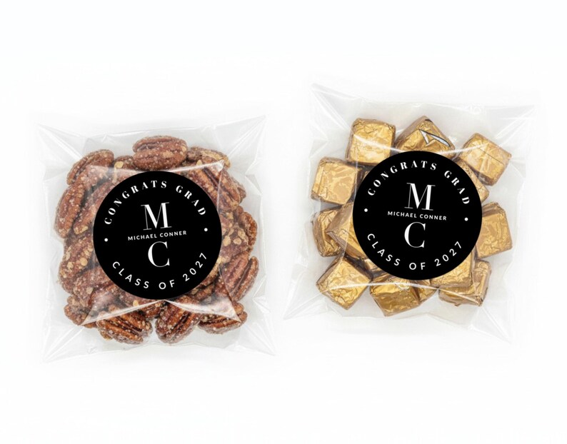 May include: Two clear cellophane bags, each containing treats. One bag holds a cluster of pecans, the other contains gold-wrapped chocolates. Both bags feature a black circular sticker with white text that reads "CONGRATS GRAD" and "CLASS OF 2027".