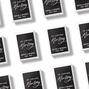 May include: A collection of rectangular white-bordered cards featuring a black background with the white text In Loving Memory, the name Kevin J. Murphy, and the years 1950-2023 printed in a combination of elegant script and sans-serif fonts.