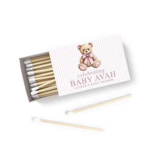a matchbox with a teddy bear on it, and there are two wooden matchsticks placed next to it.