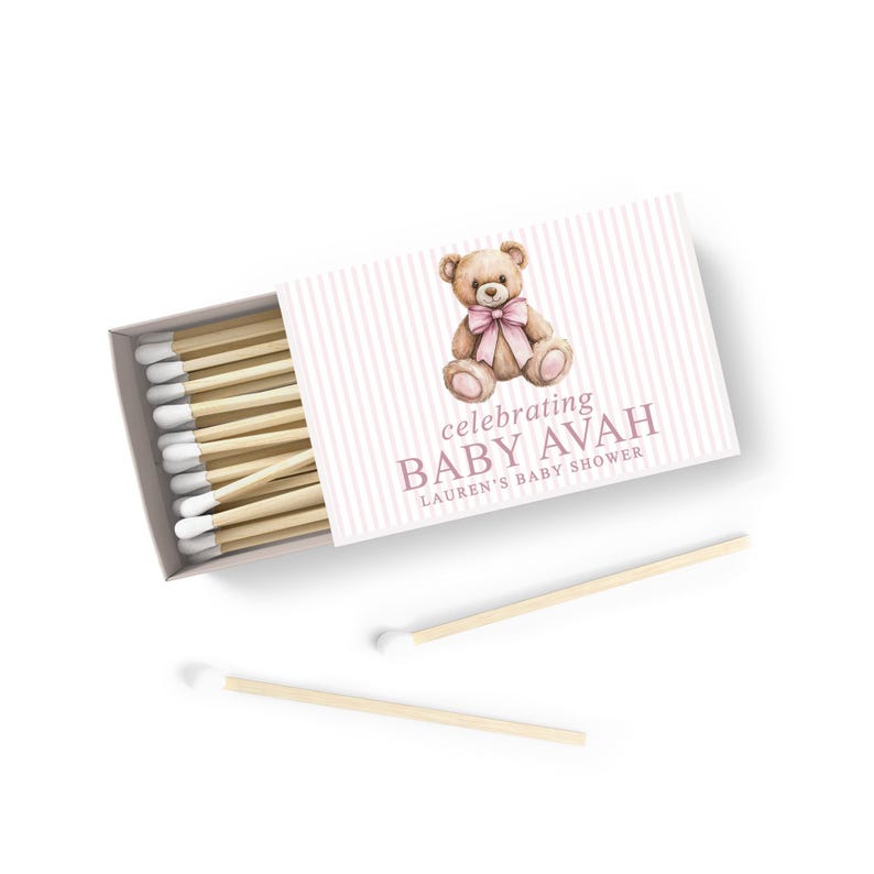a matchbox with a teddy bear on it, and there are two wooden matchsticks placed next to it.