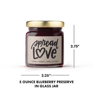 May include: A small glass jar of blueberry preserve with a gold lid. The label reads "Spread Love" with a heart, and the names Fiona & Henry, and the date April 27, 2024. The jar is 2.25 inches wide and 2.75 inches tall.