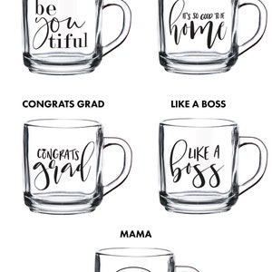 Puede incluir: Cinco tazas de vidrio diferentes con diferentes lemas impresos en ellas. Las tazas son todas de vidrio transparente con un asa negra. Los lemas en las tazas son "Beyoutiful", "It's so good to be home", "Congrats Grad", "Like a Boss" y "Mama".