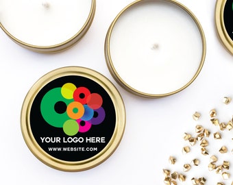 May include: Round gold metal candle tins with white wax and a central wick. One tin features a black circular label with a colorful overlapping circle graphic, the text "YOUR LOGO HERE," and "WWW.WEBSITE.COM" printed in white sans-serif font.