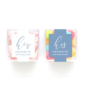 May include: Two clear acrylic boxes filled with colorful candies. One box has a white label with the text "her favorite the middleton's" and the other box has a blue label with the text "his favorite the middleton's".
