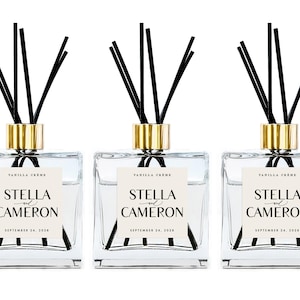 May include: Three square glass reed diffusers with gold-toned collars and black reeds. Each bottle features a cream-colored label with the text "VANILLA CRÈME", "STELLA and CAMERON", and "SEPTEMBER 24, 2028" printed in black serif and script fonts.