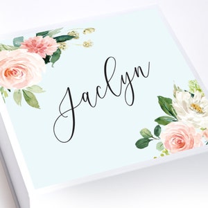 May include: A light blue gift box with a floral design and the name "Jaclyn" written in black cursive script.