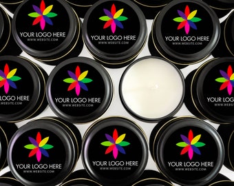 May include: A collection of round black metal candle tins with lids featuring a colorful eight-petaled flower logo, the text YOUR LOGO HERE, and WWW.WEBSITE.COM. One open tin reveals a smooth white wax surface with a centered cotton wick.