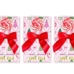 May include: Three lollipops with red and white swirls, each attached to a rectangular card featuring a pink background with a diamond pattern, green and pink Christmas trees, and a red bow. The text reads MERRY CHRISTMAS LOVE ELLA.