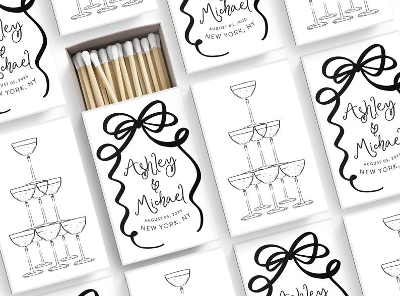 May include: White matchboxes with black and white illustrations of champagne glasses and a bow. The text on the matchboxes reads "Ashley & Michael" and includes the date and location of the wedding.