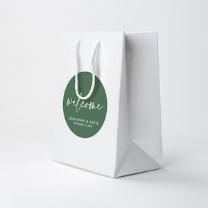A white paper bag with a green circular sticker that says "Welcome Jonathan & Kate September 16, 2020" printed on it.