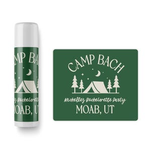 May include: A green square sticker with the text "Camp Bach" in white, a white tent icon, and the text "Michelle's Bachelorette Party Moab, UT". A white lip balm tube with the same text and icon is also shown.