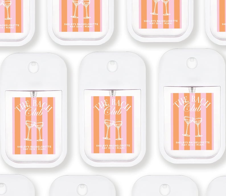 multiple white spray bottles with orange and pink striped labels, each featuring a graphic of two champagne glasses and the text "The Bach Club" and "Shelley's Bachelorette May 12, Miami".