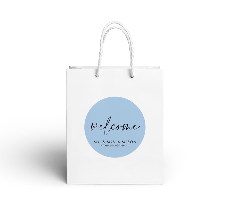 A white paper shopping bag with a blue circular logo and the text "welcome Mr. & Mrs. Simpson" printed on it.