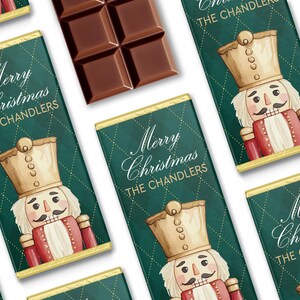 May include: Chocolate bars with a dark green and gold design. The bars feature a watercolor illustration of a nutcracker and the text "Merry Christmas THE CHANDLERS". A piece of chocolate is visible.