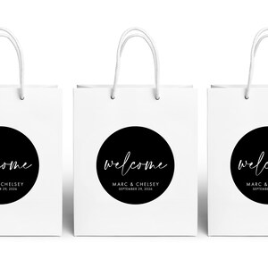 Three white paper bags with black text and logos, including a welcome message and the names Marc & Chelsea.