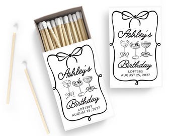 May include: A white matchbox and a separate card with a black and white design. The design includes the text "Ashley's Birthday" and illustrations of cocktail glasses. The matchbox contains wooden matches with white tips.